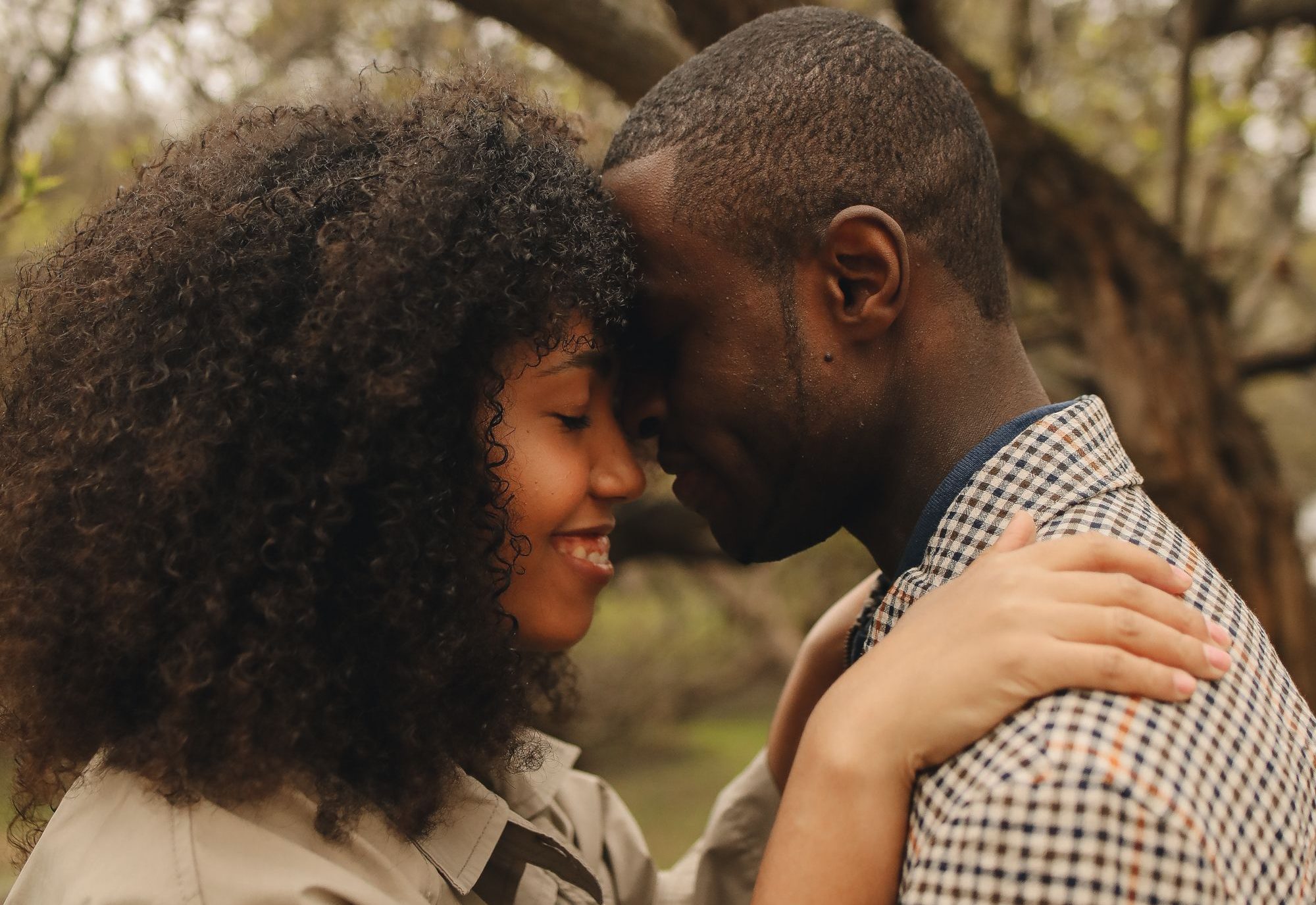 A couple resting their foreheads together under a tree