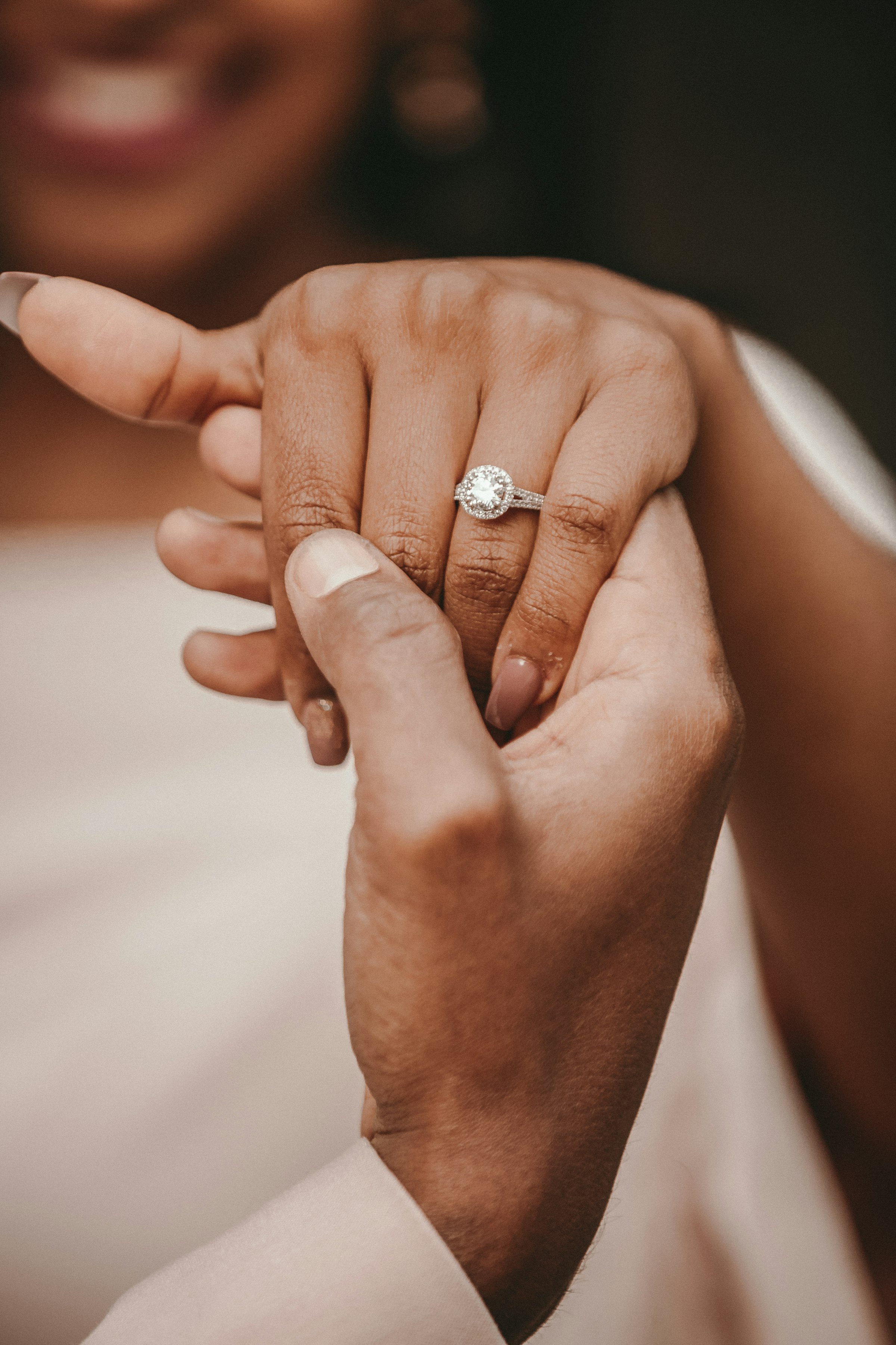 Two hands clasped, one wearing an engagement ring